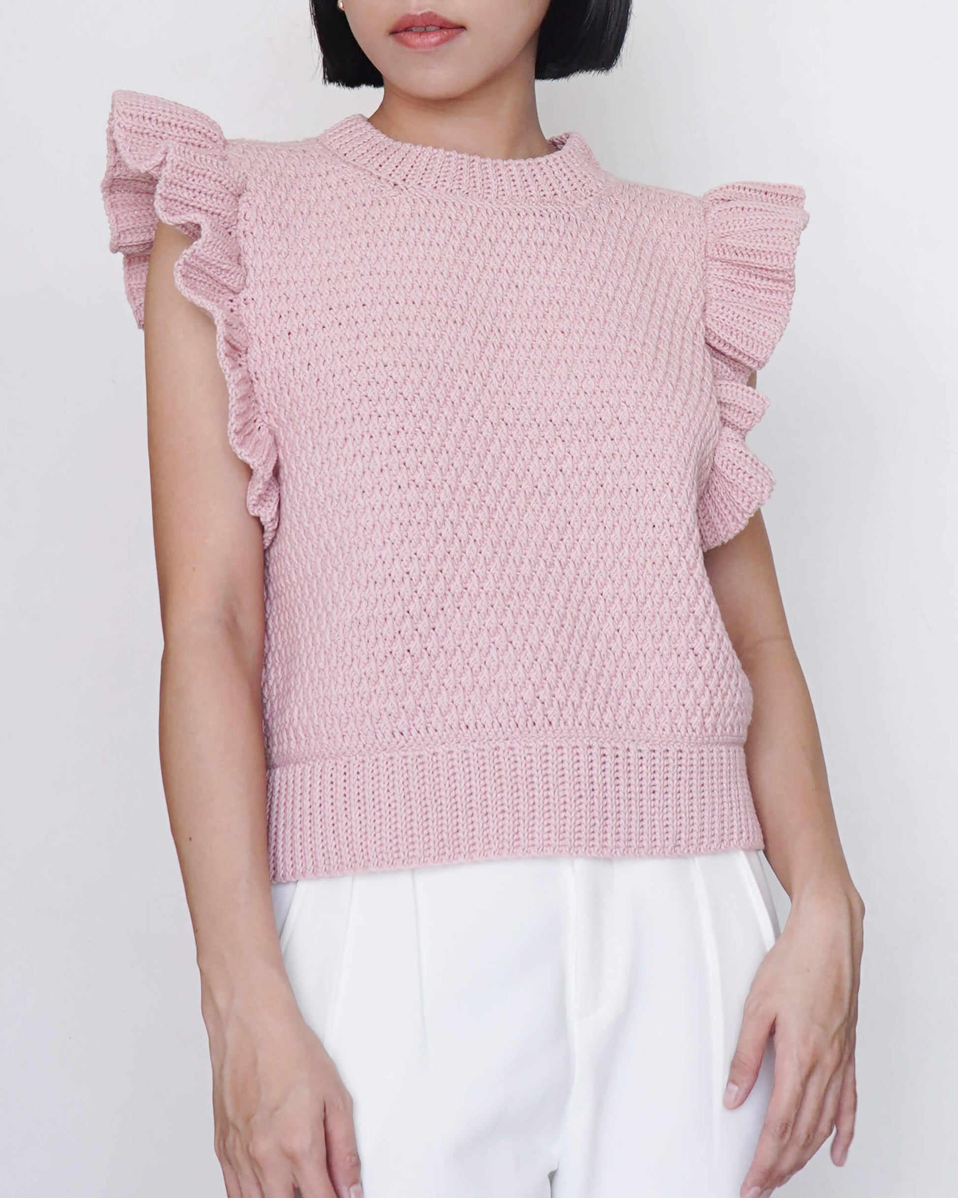 Person wearing a pink knitted top with ruffled sleeves on a white background