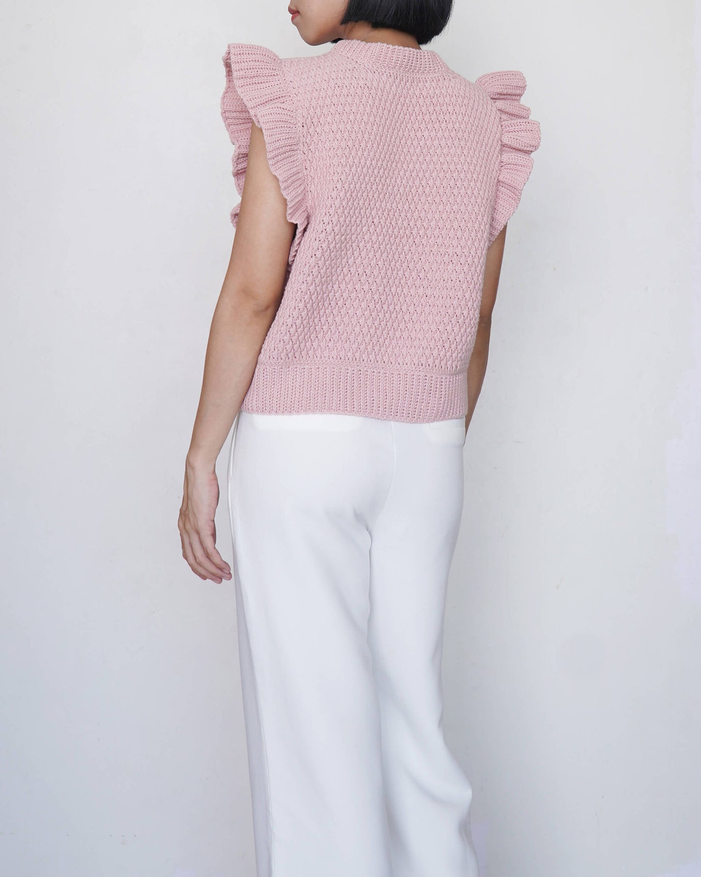 Person wearing a pink crochet top with ruffled sleeves on a white background